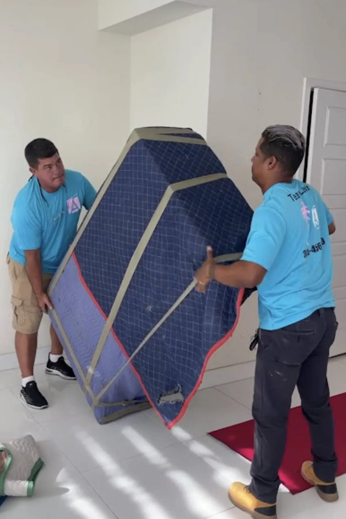 Two Allen & Son movers carrying a wrapped piece of furniture in company t-shirts